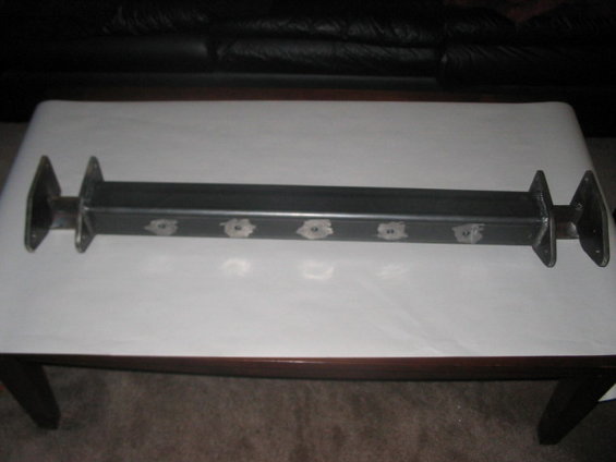 Custom metal axle with flange mounts on each end and six bolt holes along the body