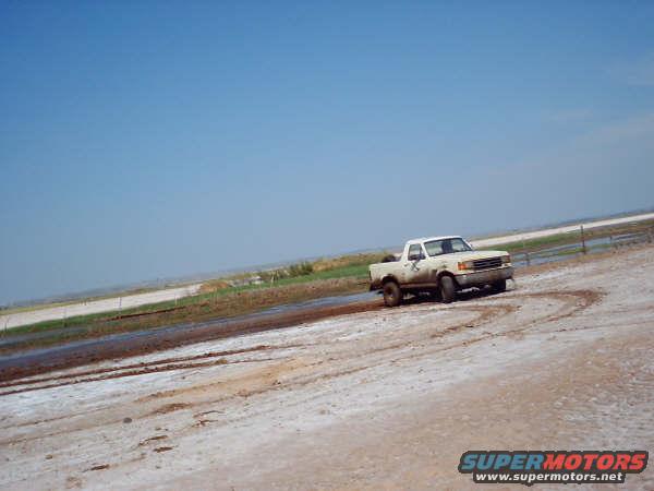 White 1991 Ford Bronco driving on a dirt road, front 3/4 view
