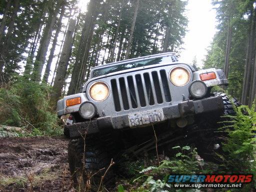 Silver Jeep Wrangler on a muddy forest trail, tires are angled