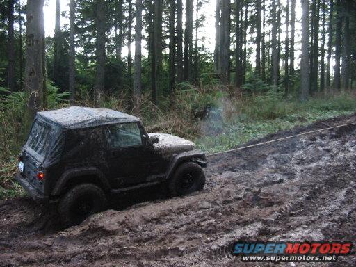 Mud-covered Jeep Wrangler being towed on a muddy forest track