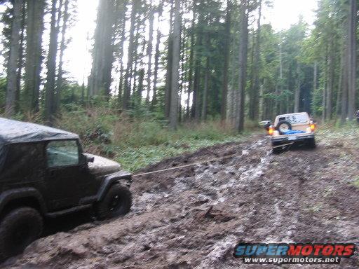 Two off-road vehicles stuck in mud, one being towed