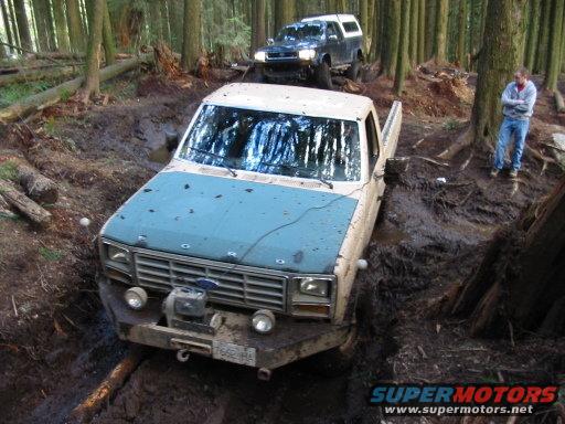 Ford F-150 stuck in a muddy forest trail with another truck behind it