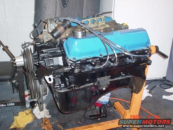 Engine on an orange stand, with blue valve covers and black block. Wires and hoses are connected