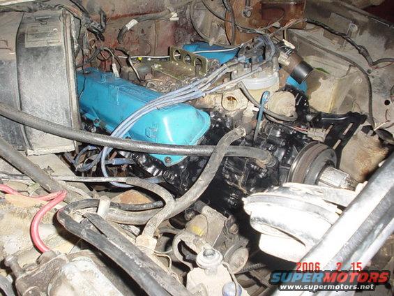 Engine bay with blue valve covers and black engine block, showing hoses and wiring
