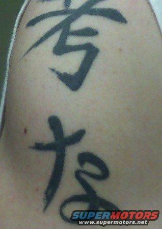 Close-up of a black tattoo with Japanese characters on skin. Supermotors.net logo visible at bottom