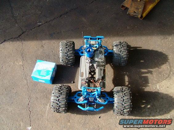 blue remote control monster truck with large tires sitting on concrete next to a box