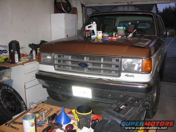 Front view of a brown and white 1987 Ford Bronco parked in a garage with parts and tools on the hood