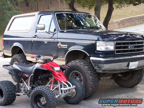 1991 Ford Bronco with lifted suspension parked next to a red ATV