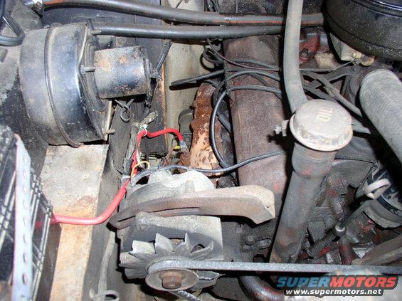 Engine bay close-up showing alternator, brake booster, and exhaust manifold. Oil fill cap visible