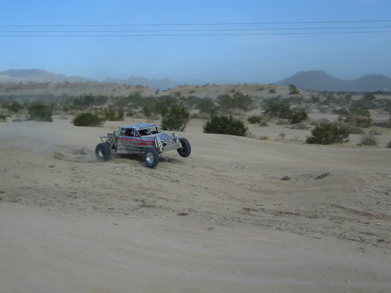 Off-road buggy kicking up dust on a sandy trail with desert brush and mountains in the background