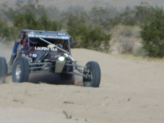 Off-road buggy with number 1007 on roof, driving on sand