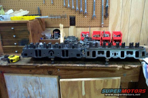 Two engine cylinder heads on a workbench with tools and parts in the background