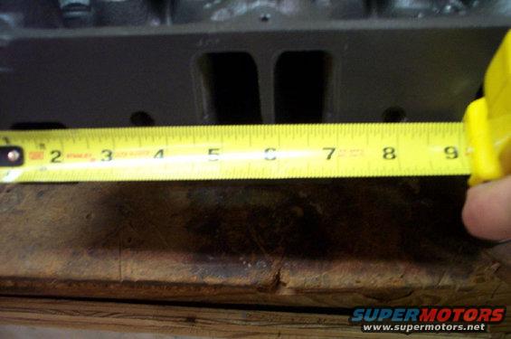 Engine cylinder head being measured with a yellow tape measure. Numbers 2 through 9 are visible