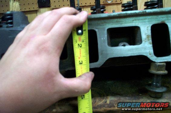 Hand holding tape measure against engine cylinder head, showing about 2.5 inches