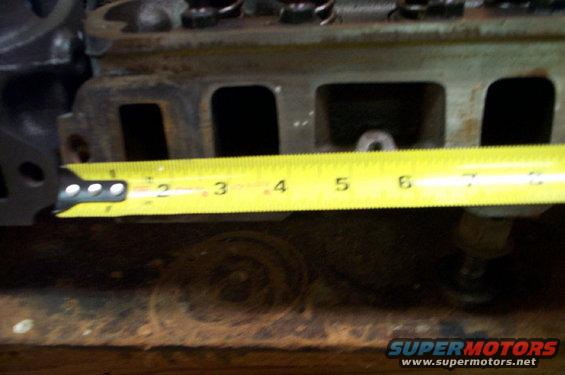 Engine cylinder head with a yellow measuring tape showing approximately 3.5 inches