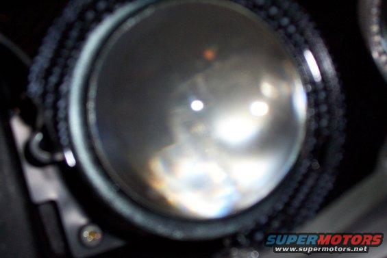 Close-up of a car headlight projector lens with internal reflections and a textured black bezel