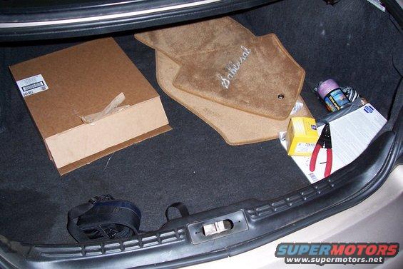 Trunk interior with 'Sable' floor mats, cardboard box, and tools