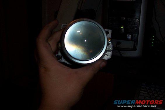 Hand holding a round headlight projector lens, showing reflections on the glass