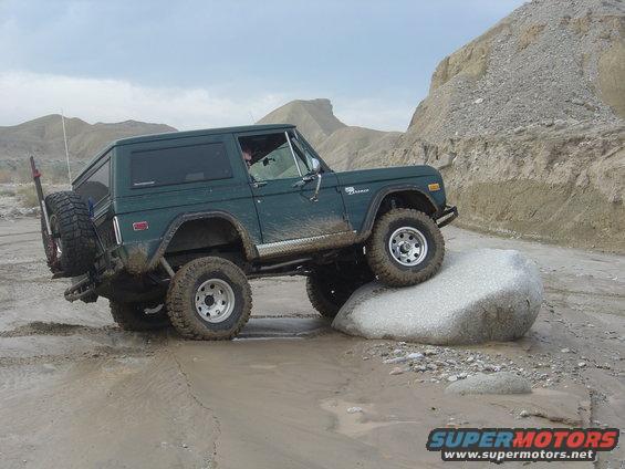 Green 1972 Ford Bronco navigating off-road terrain, tires on a large rock
