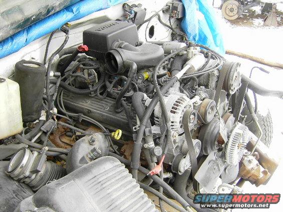 Engine assembly with various hoses, belts, and components. A blue tarp is visible in the background