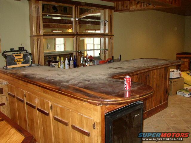 Home bar interior with horseshoe counter, bottles, and mini-fridge. Coca-Cola can on counter