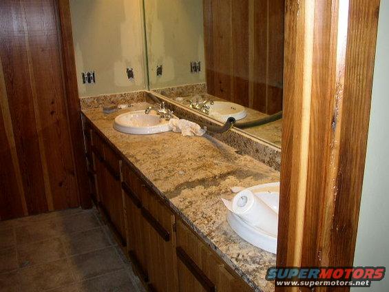 Bathroom vanity with granite countertop, two sinks, and wooden cabinets