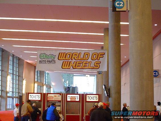 People at ticket booths inside a building with a banner that says "O'Reilly Auto Parts World of Wheels"