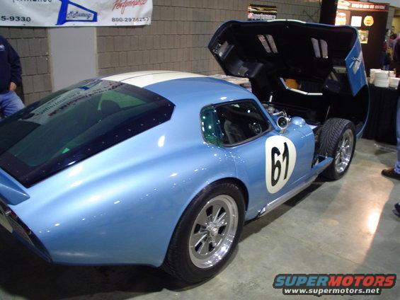 Blue race car with white stripes, number 61 on door, hood open, seen from the rear three-quarter angle