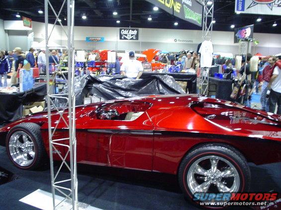 Red custom hot rod with chrome wheels and red pinstripes, seen from the side at a car show