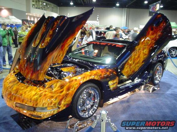 Dark blue Chevrolet Corvette with custom flame paint on hood, doors, and fenders. Hood and doors are open. Chrome wheels visible