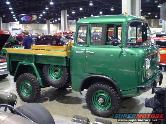 Green pickup truck with side-mounted spare tires and wooden bed