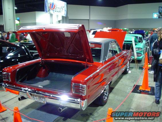 Red classic car with trunk open, parked indoors next to other vehicles
