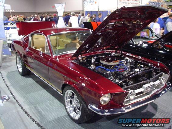 Maroon 1967 Ford Mustang coupe with tan interior, chrome wheels, and engine exposed
