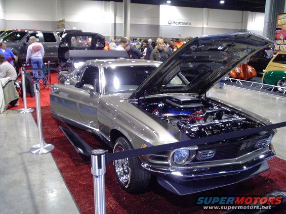 1969 Ford Mustang Mach 1 with hood open, showing engine. Car is tan with chrome accents