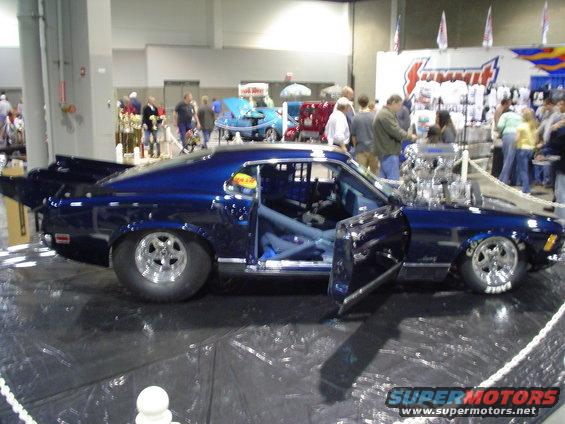 Blue custom drag car with exposed engine and roll cage, doors open, on display