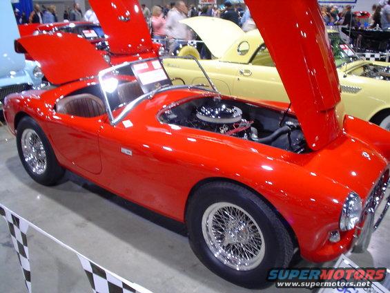 Red sports car with wire wheels and open hood showing engine, parked indoors