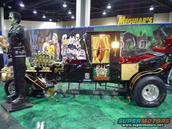 Frankenstein figure next to a black carriage car with a V8 engine and gold trim