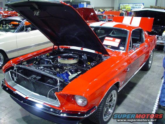 Orange 1967 Ford Mustang fastback with hood open, showing engine and racing stripes