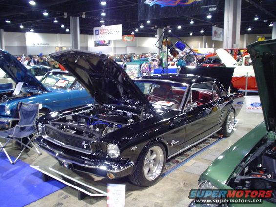 Black 1965 Ford Mustang coupe with hood open, red interior, and custom wheels