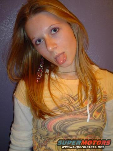 Woman with blonde hair sticking her tongue out, wearing a yellow shirt with a graphic print