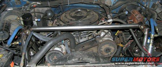 Engine bay with a metal brace across the top, blue hoses, and various engine components visible