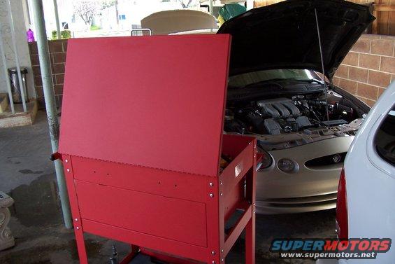 Silver sedan with hood open, showing V6 engine. Red toolbox in foreground