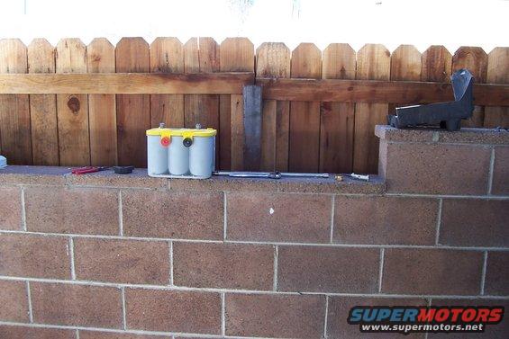 Optima battery on a brick wall in front of a wooden fence