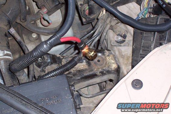 Engine bay wiring with red battery cable connected to a brass terminal, black plastic fuse box visible