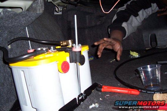 Car battery being installed in trunk, with tools and a cup nearby