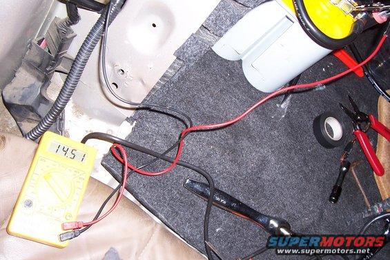 Car interior with yellow multimeter reading 14.51, red and black wires, tape, and pliers
