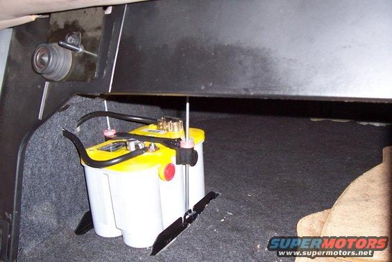 Optima yellow top battery with red caps, secured in a car trunk with carpet lining