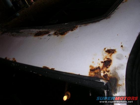 White car body panel with extensive rust damage along the seam and edge