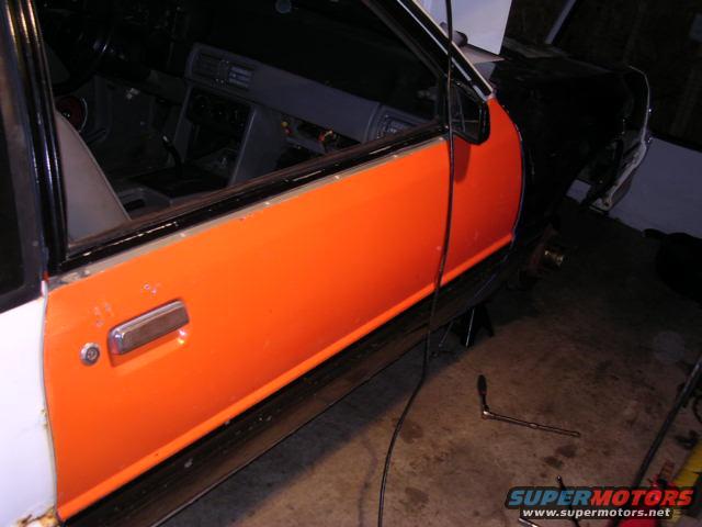 car door with orange panel, interior visible, car on jack stands