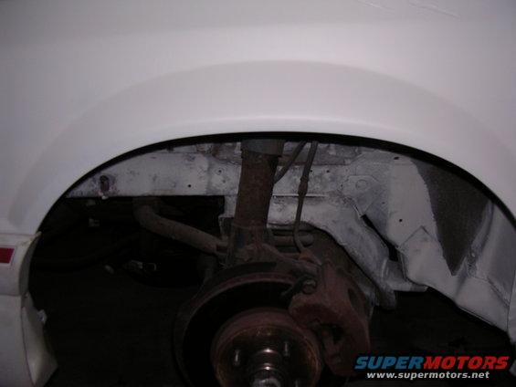 White 1988 Ford Mustang front wheel well with rusty suspension components and brake rotor